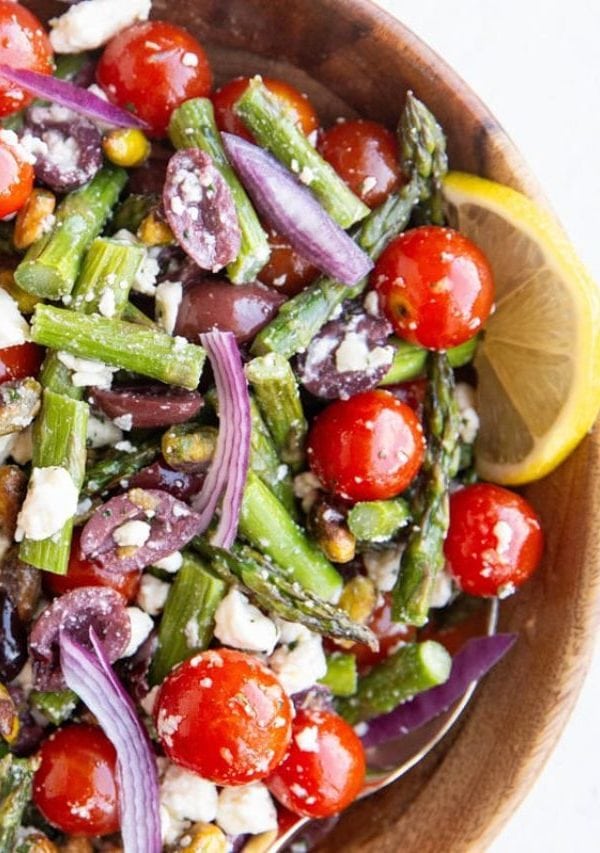 Wooden bowl full of asparagus salad with tomatoes, ready to serve.