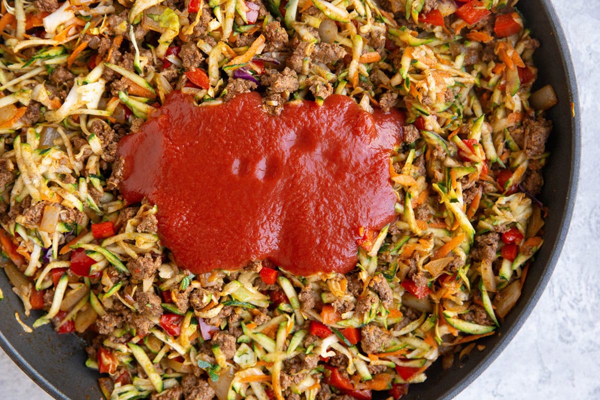 Tomato sauce on top of ground beef and vegetables in a skillet.