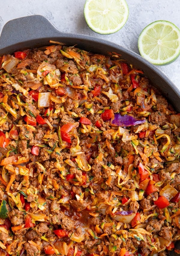 Skillet full of ground beef and vegetables with fresh limes to the side, ready to serve.