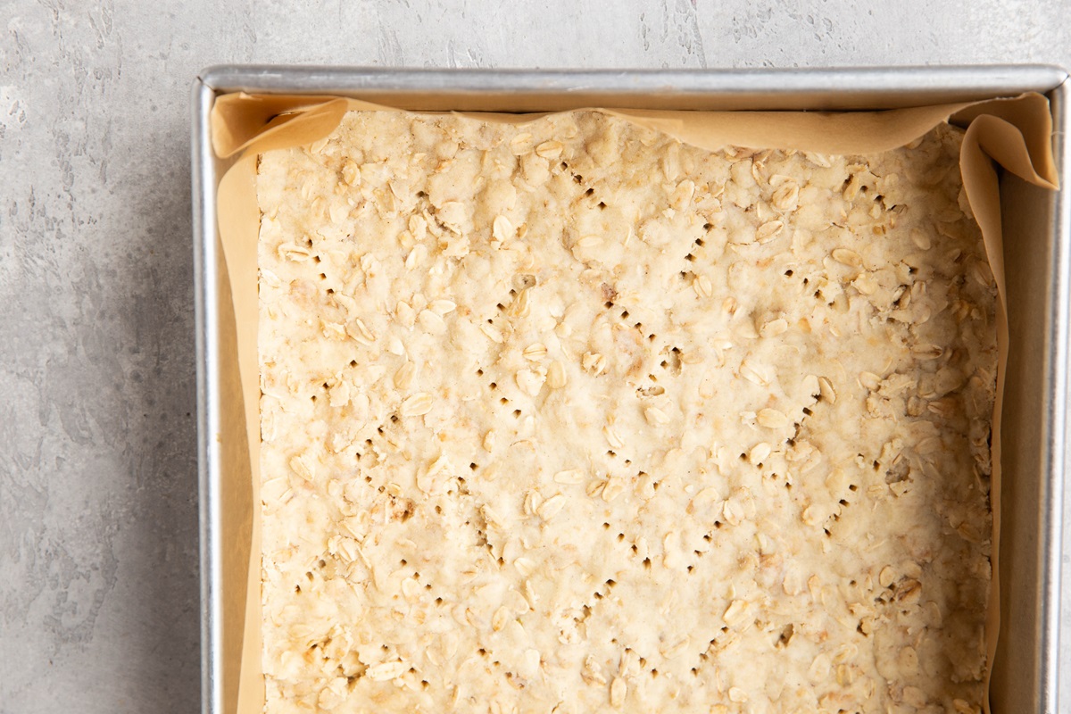 Crust mixture inside of a square baking pan, ready to go into the oven to pre-bake.
