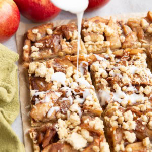 Spoon drizzling glaze over sliced apple crumb bars.