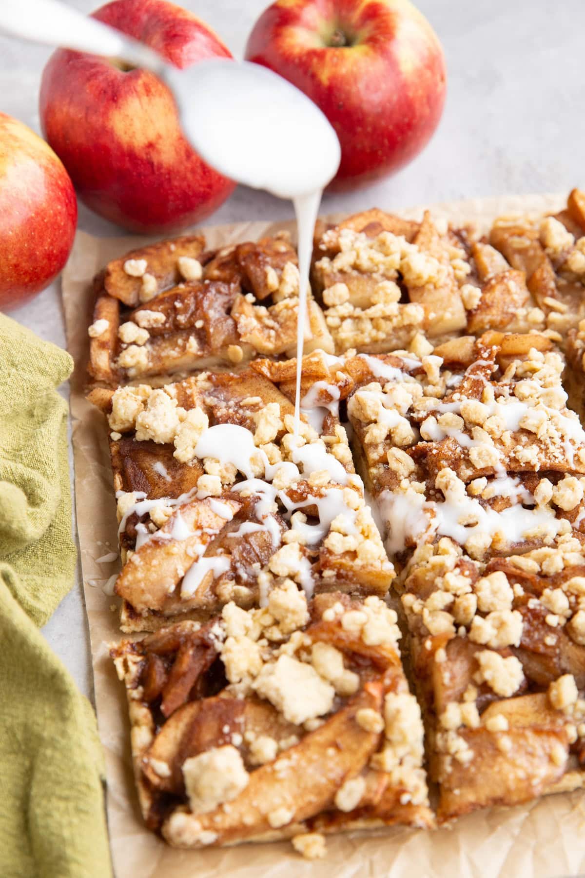 Spoon drizzling glaze over sliced apple crumb bars.