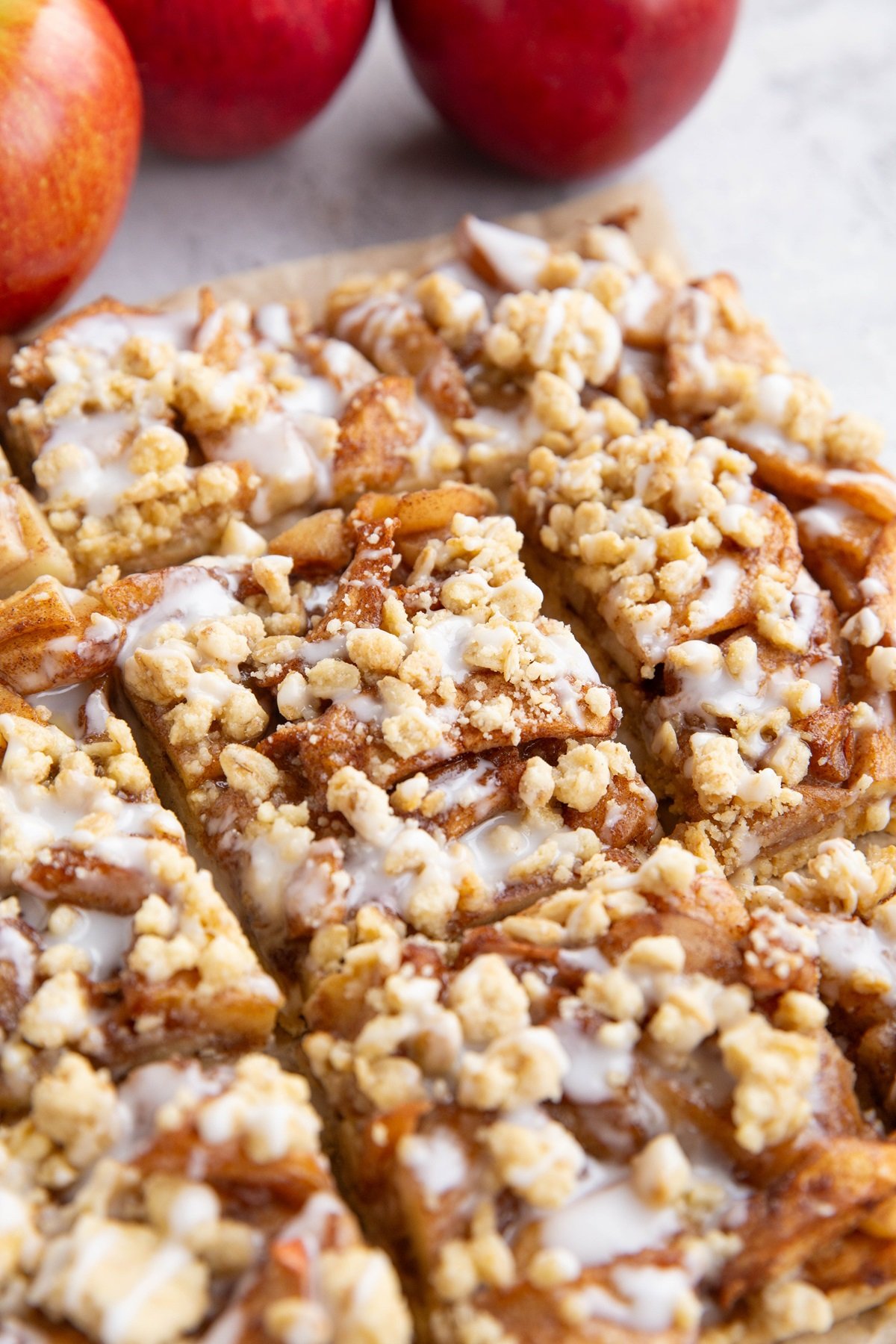 Apple crumb bars on a sheet of parchment paper, cut into slices. Fresh apples in the background.