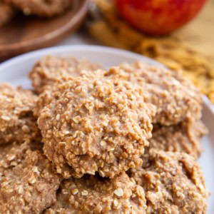 White plate of applesauce cookies with an apple in the background.