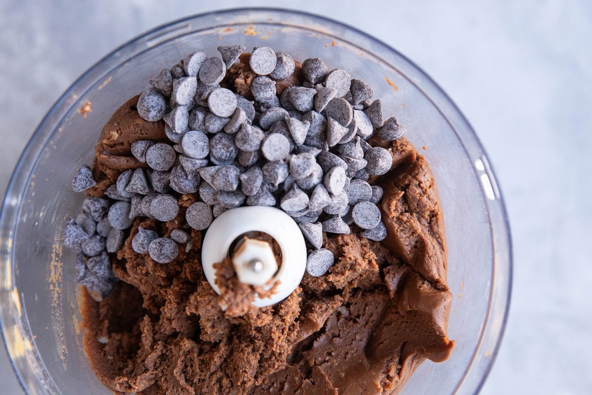 Chocolate chips on top of chickpea cookie dough in a food processor.