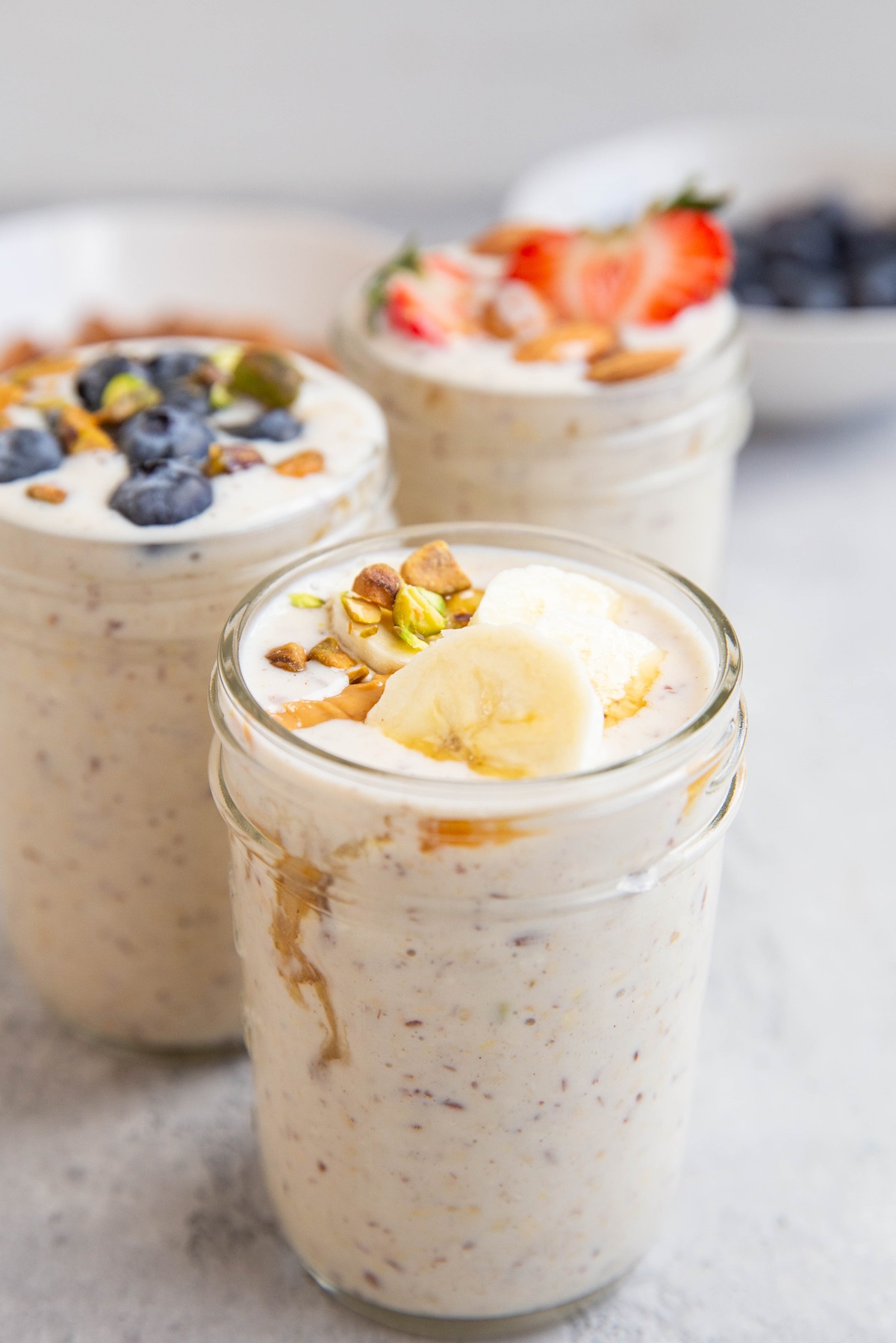 Three jars of overnight oats with fresh fruit on top, ready to eat.