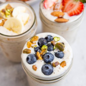 Three jars of overnight oats. One with blueberries on top, one with strawberries, and one with sliced bananas.