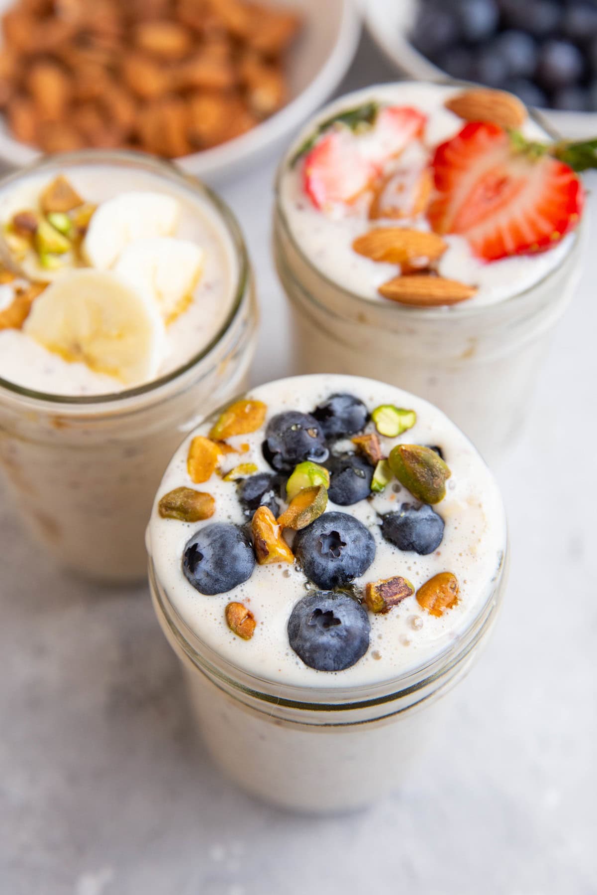 Three jars of overnight oats. One with blueberries on top, one with strawberries, and one with sliced bananas.