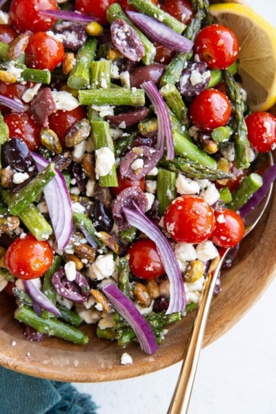 Variety of summer salads on a table, including summer pasta salad, summer fruit salad, and a leafy green summer salad with fresh strawberries.