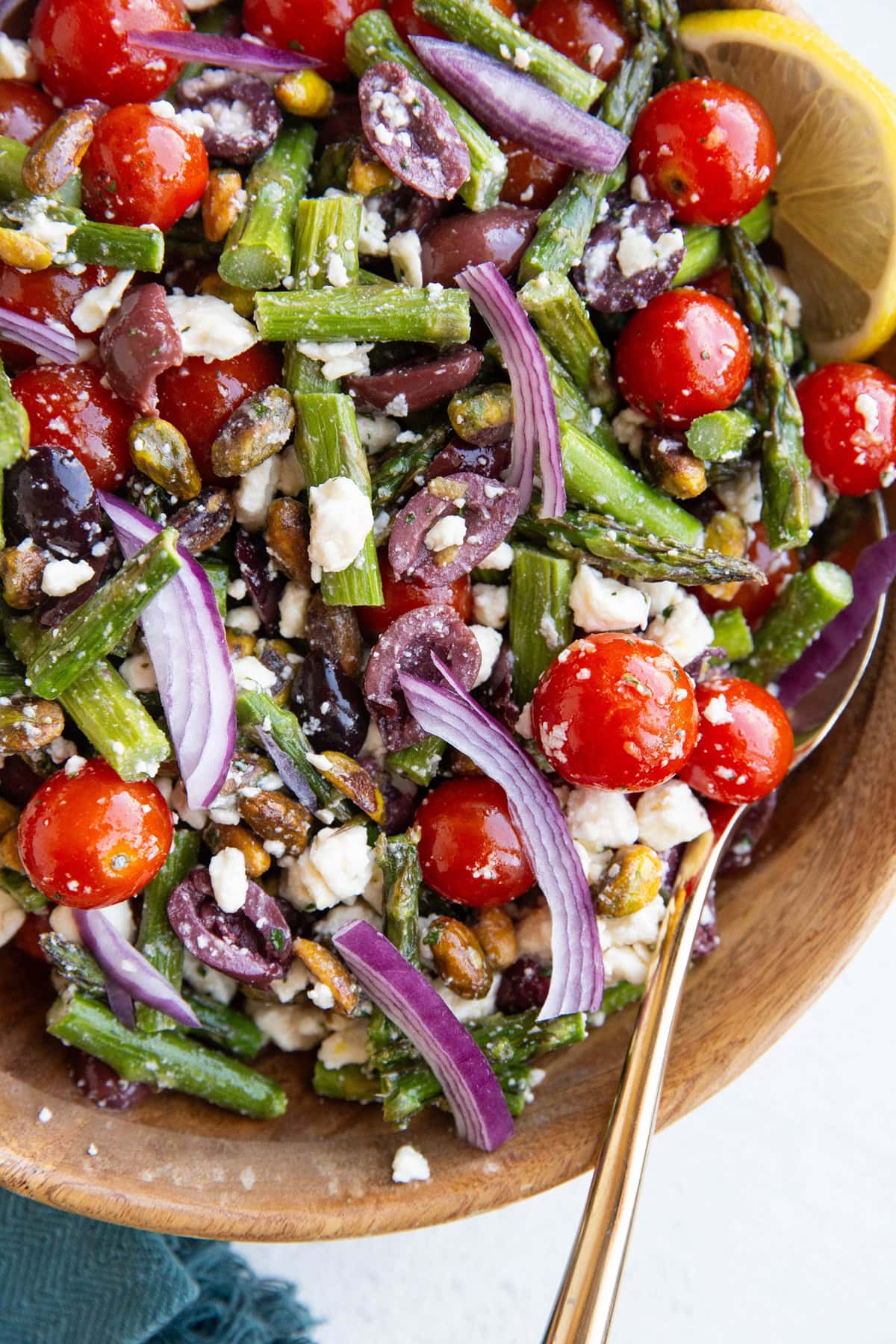 Big wood bowl of asparagus salad with a spoon for serving and a blue napkin to the side.