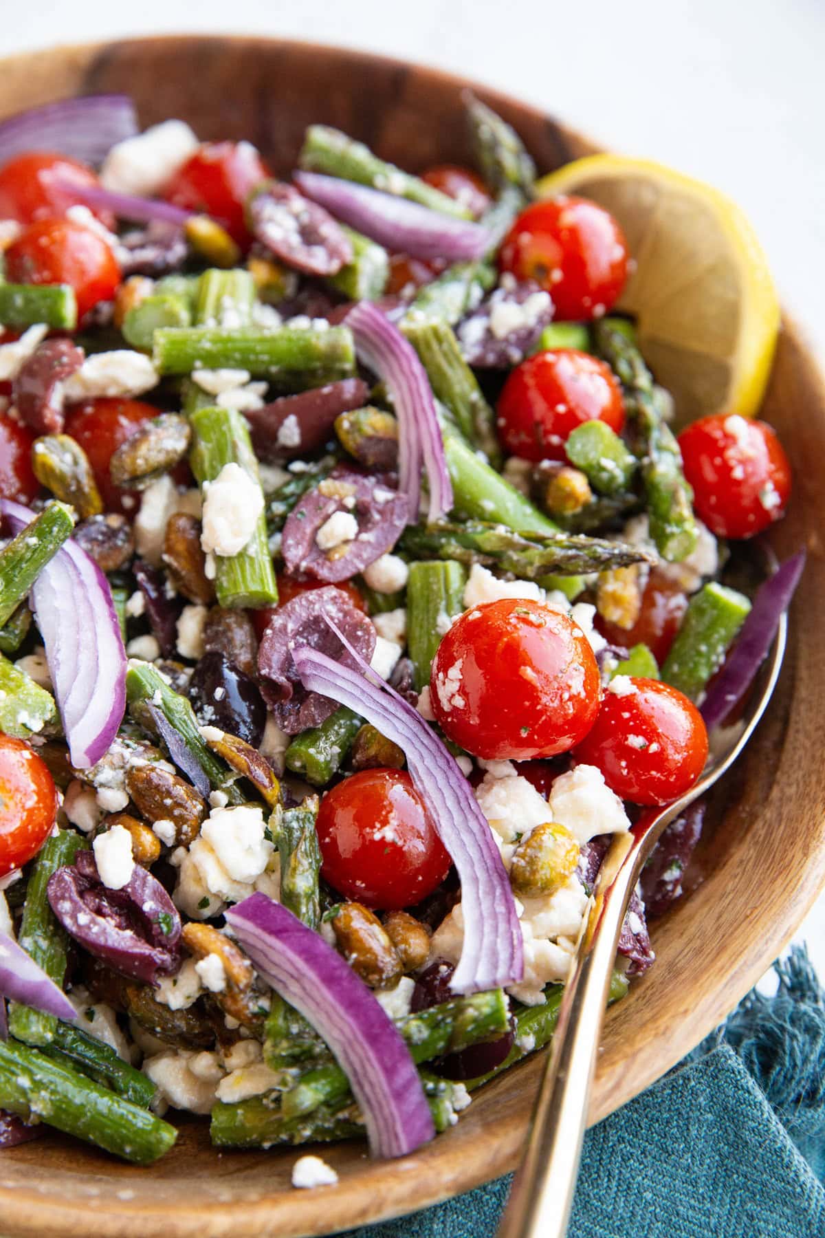 Big wooden bowl of asparagus salad with a spoon for serving and a blue napkin to the side.