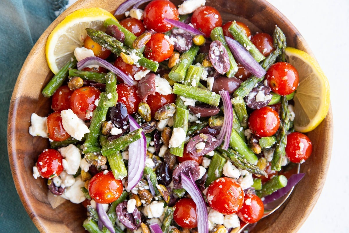 Wooden bowl full of asparagus salad with tomatoes, ready to serve.