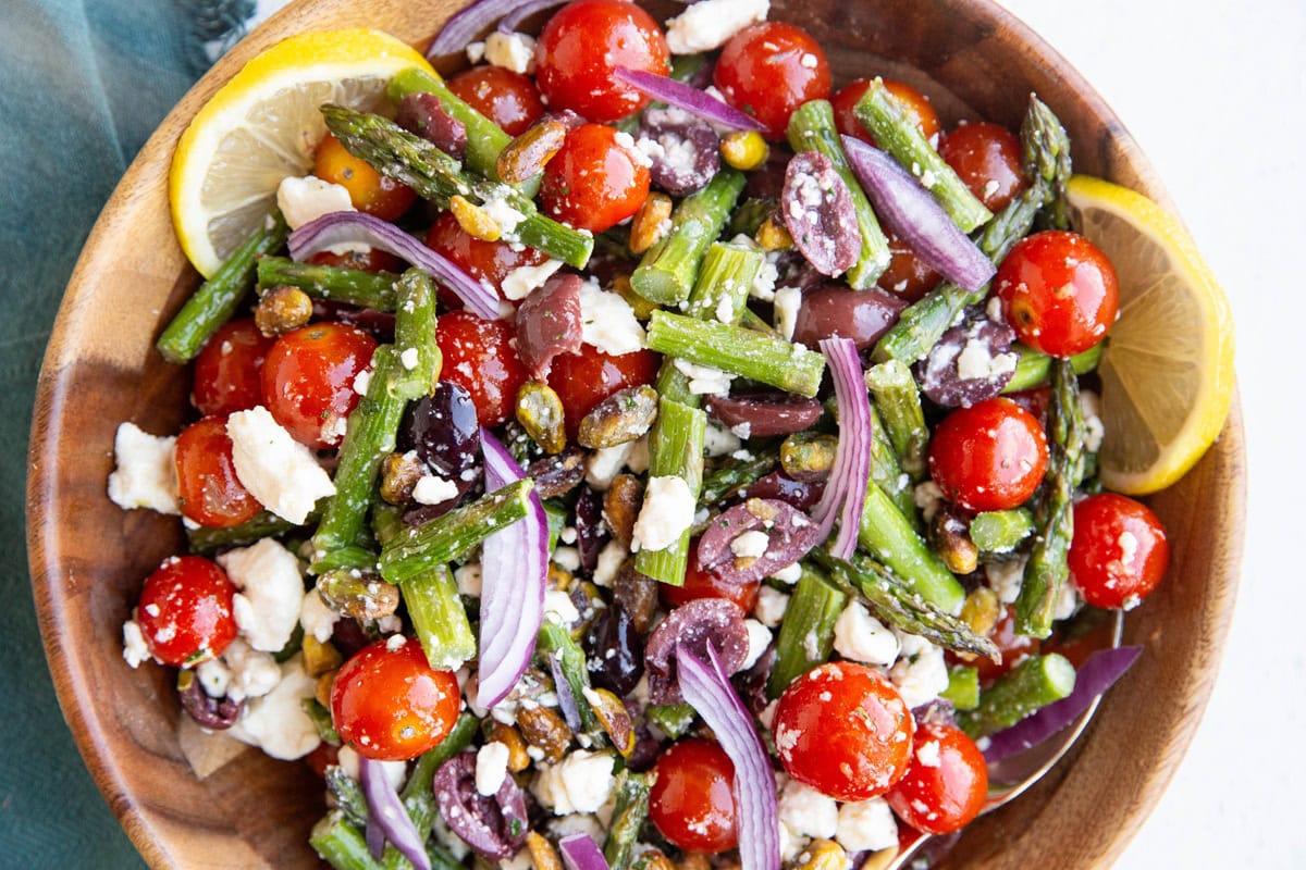 Wooden bowl full of asparagus salad with tomatoes, ready to serve.