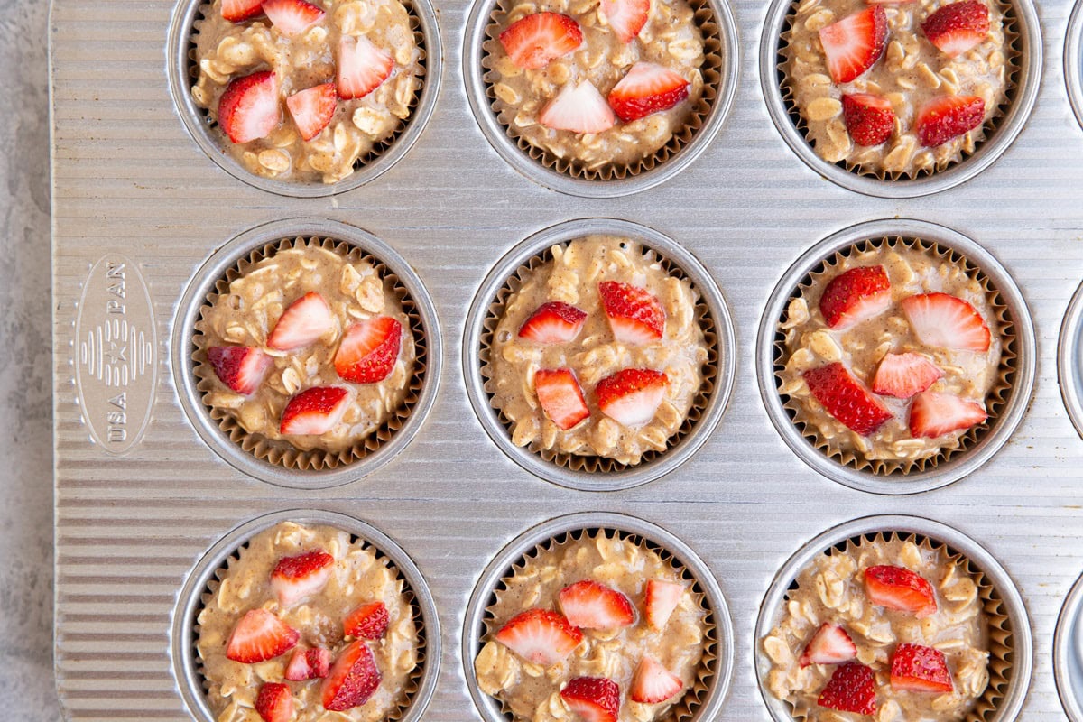 Muffin tin with strawberry banana oatmeal muffin batter inside of paper liners, ready to go into the oven.