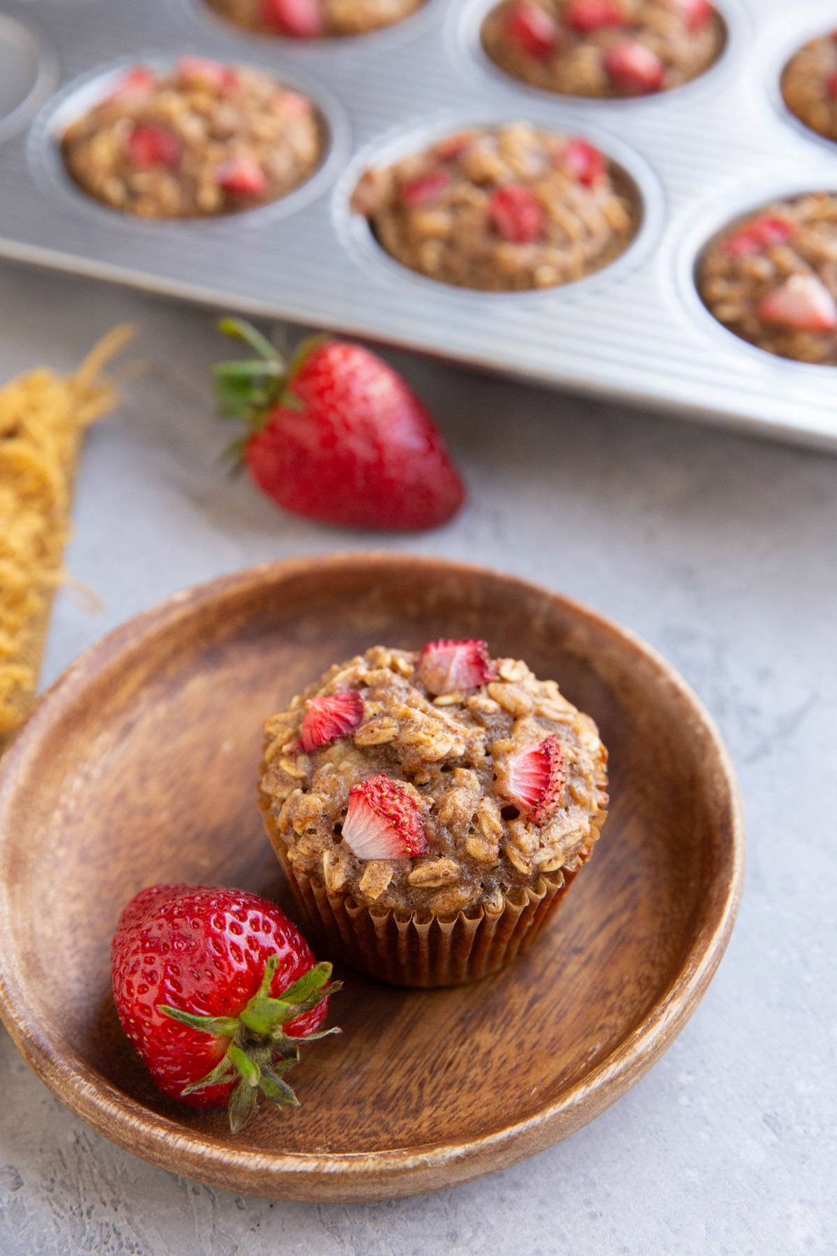 Strawberry oatmeal banana muffin on a wooden plate with the rest of the muffins in the muffin tray in the background.