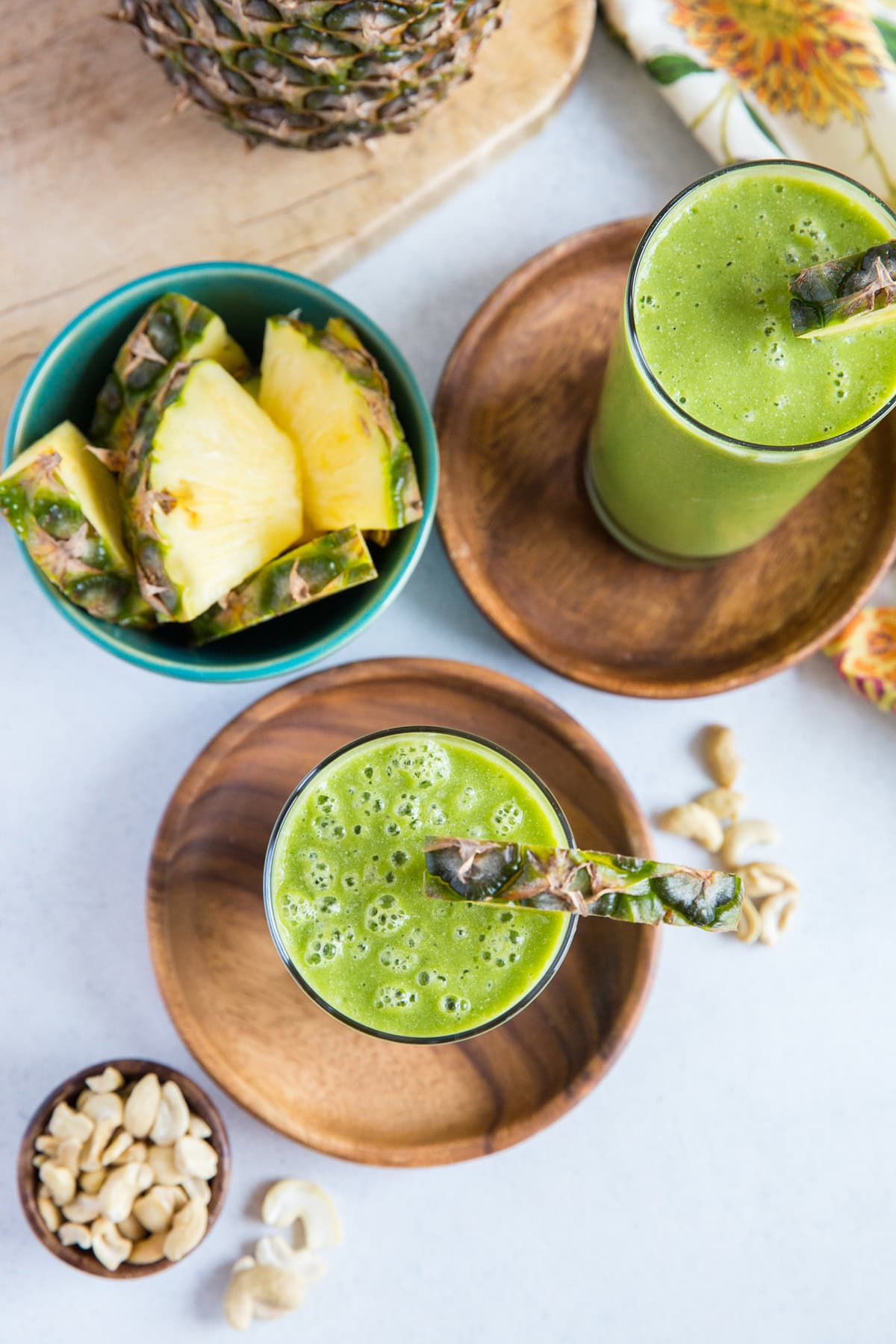 Two glasses of tropical smoothies on a white background with a bowl of fresh pineapple to the side.