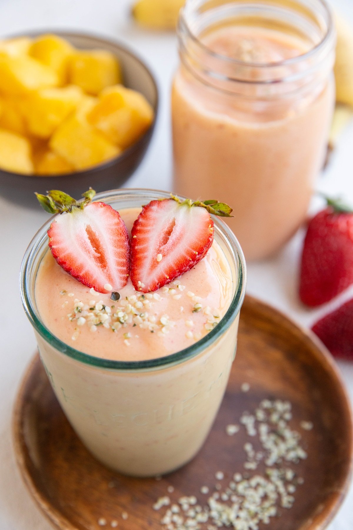 Tropical smoothies in two glasses with sliced strawberries and hemp seeds on top.