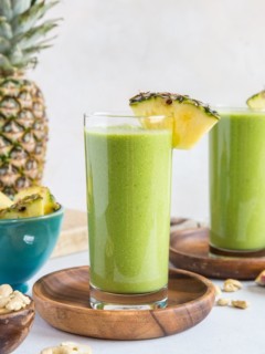 Two green smoothies in glasses with fresh pineapple garnishing the glass