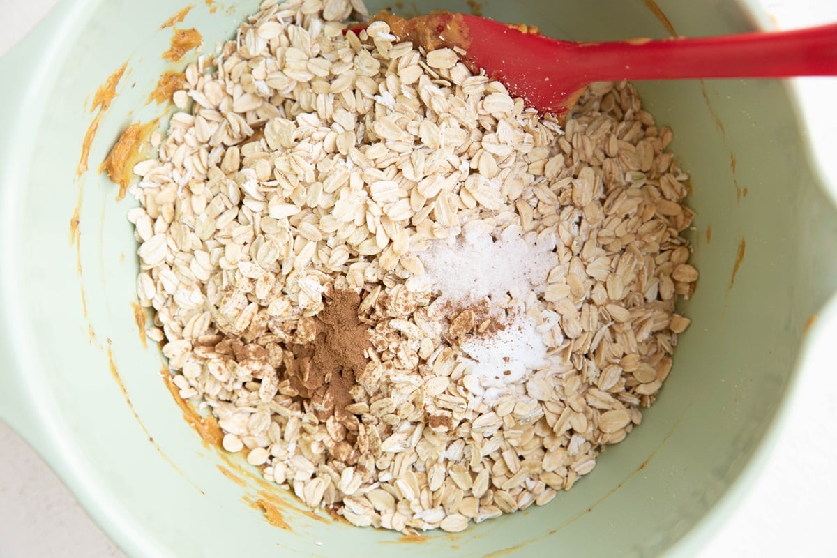 Mixing bowl with oats, cinnamon, and salt on top of peanut butter mixture in a mixing bowl.