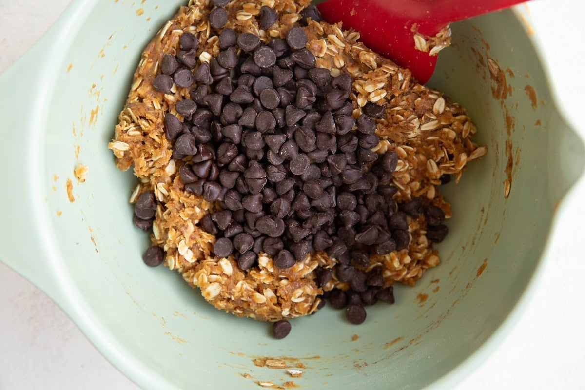 Mixing bowl with peanut butter oatmeal chocolate chip cookie dough with chocolate chips on top of the dough ready to be mixed in.