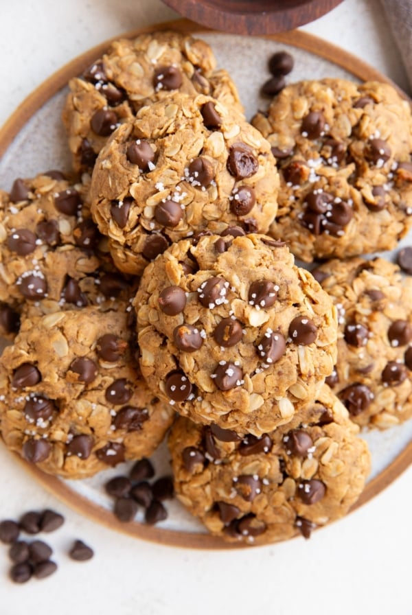 Plate of vegan chocolate chip oatmeal cookies sprinkled with sea salt and chocolate chips sprinkled around.