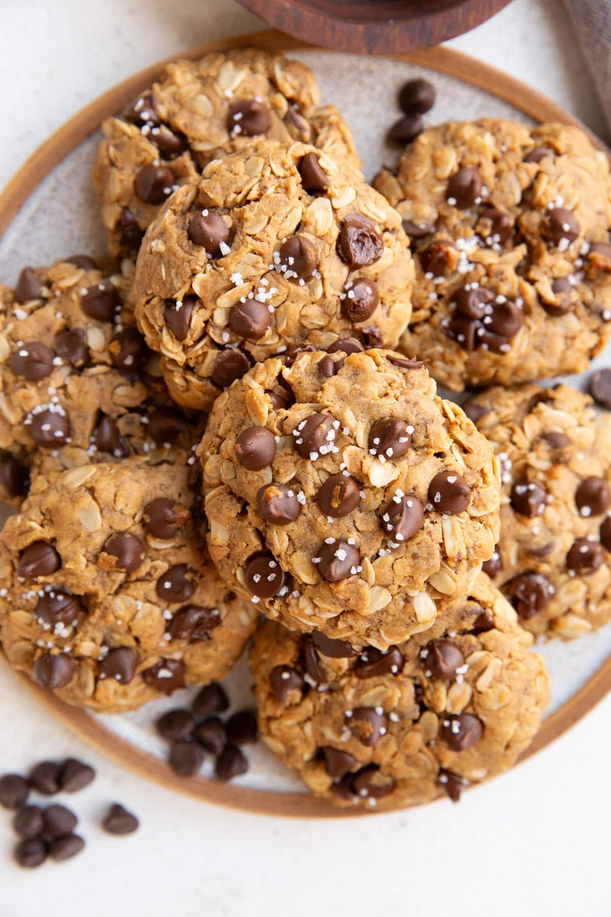 Plate of vegan chocolate chip oatmeal cookies sprinkled with sea salt and chocolate chips sprinkled around.