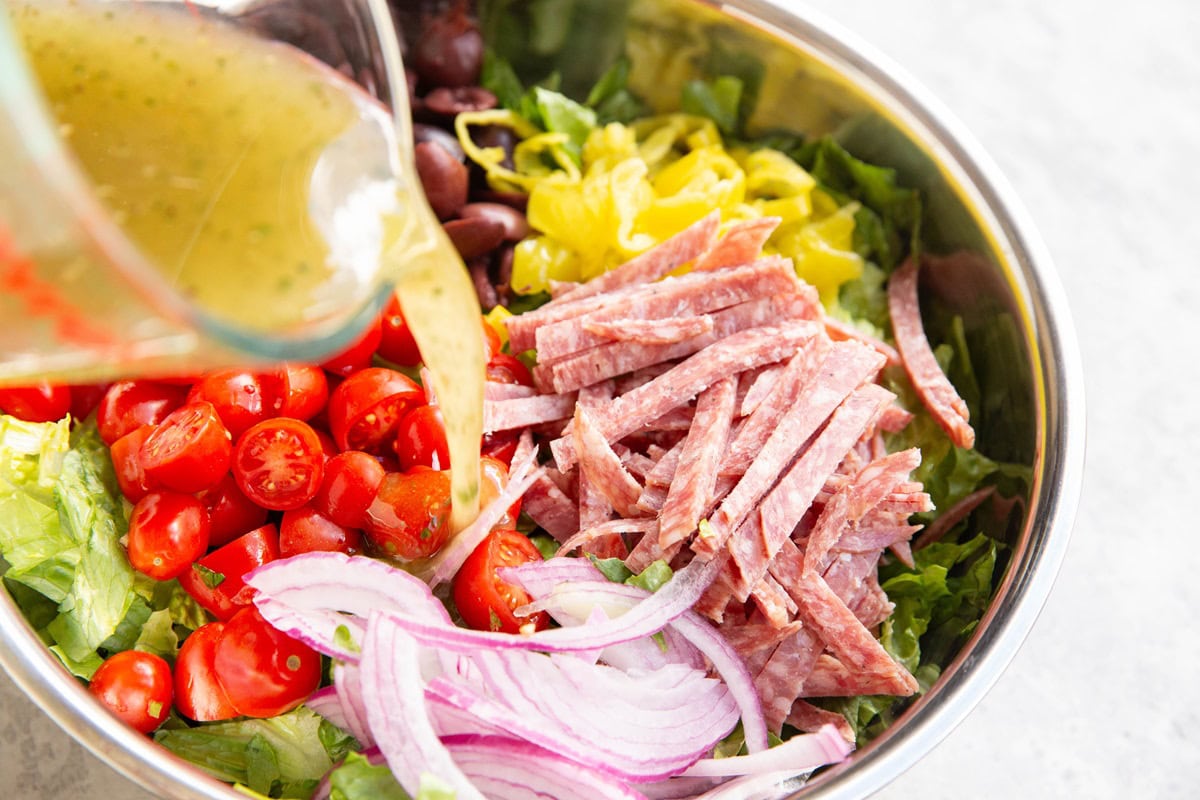 Pouring salad dressing into the bowl with the salad ingredients.