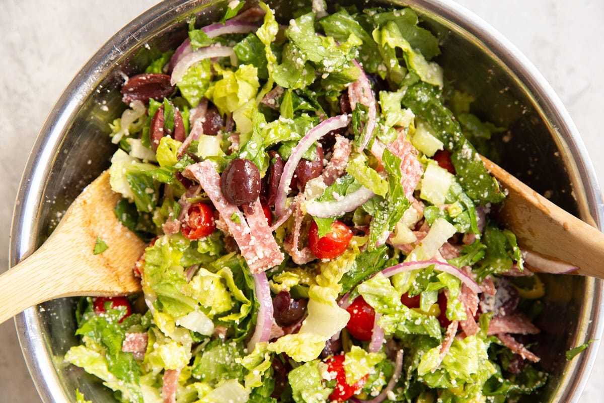 Large bowl of Italian salad with wooden spoons to the side, freshly tossed.