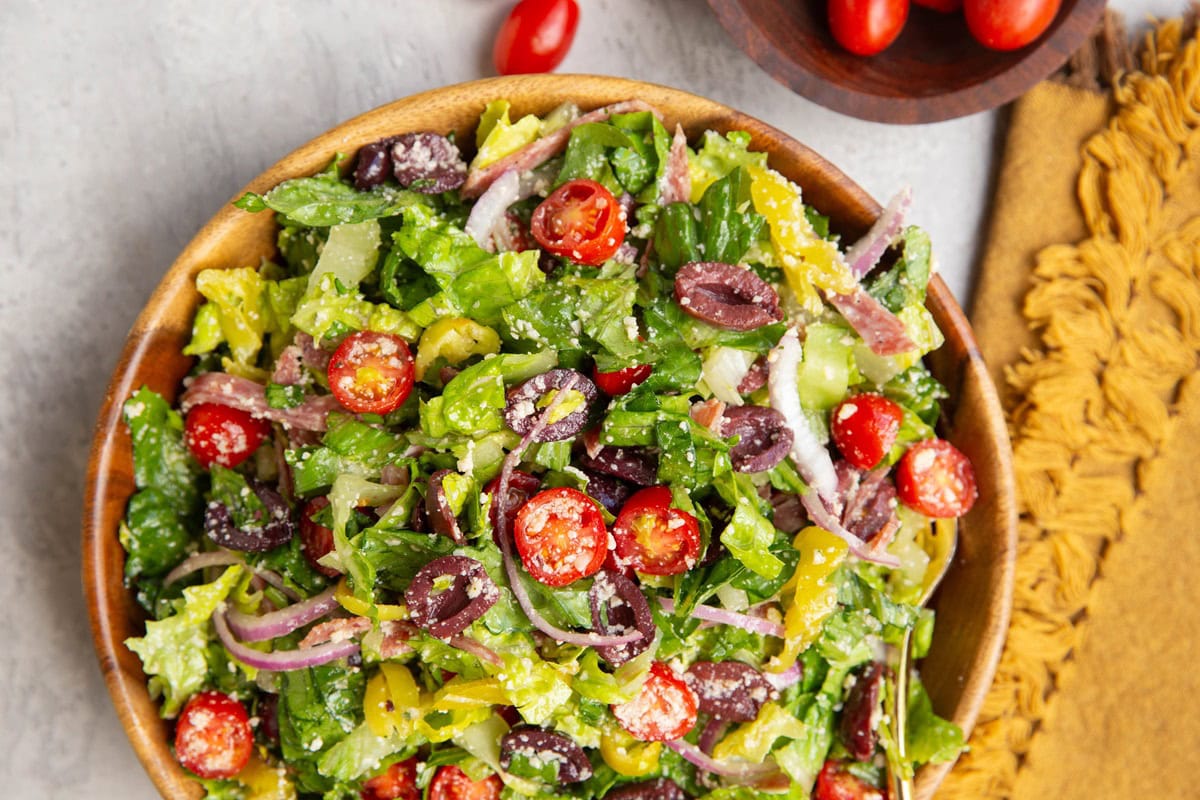 Wooden serving bowl full of Italian chopped salad with a napkin to the side and a bowl of cherry tomatoes.