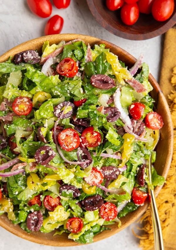 Big bowl with a big Italian salad inside with fresh tomatoes, olives, onions, and more.