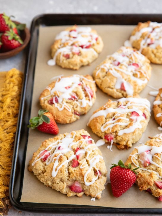 Baking sheet of almond flour strawberry scones with fresh strawberries and a napkin to the side.