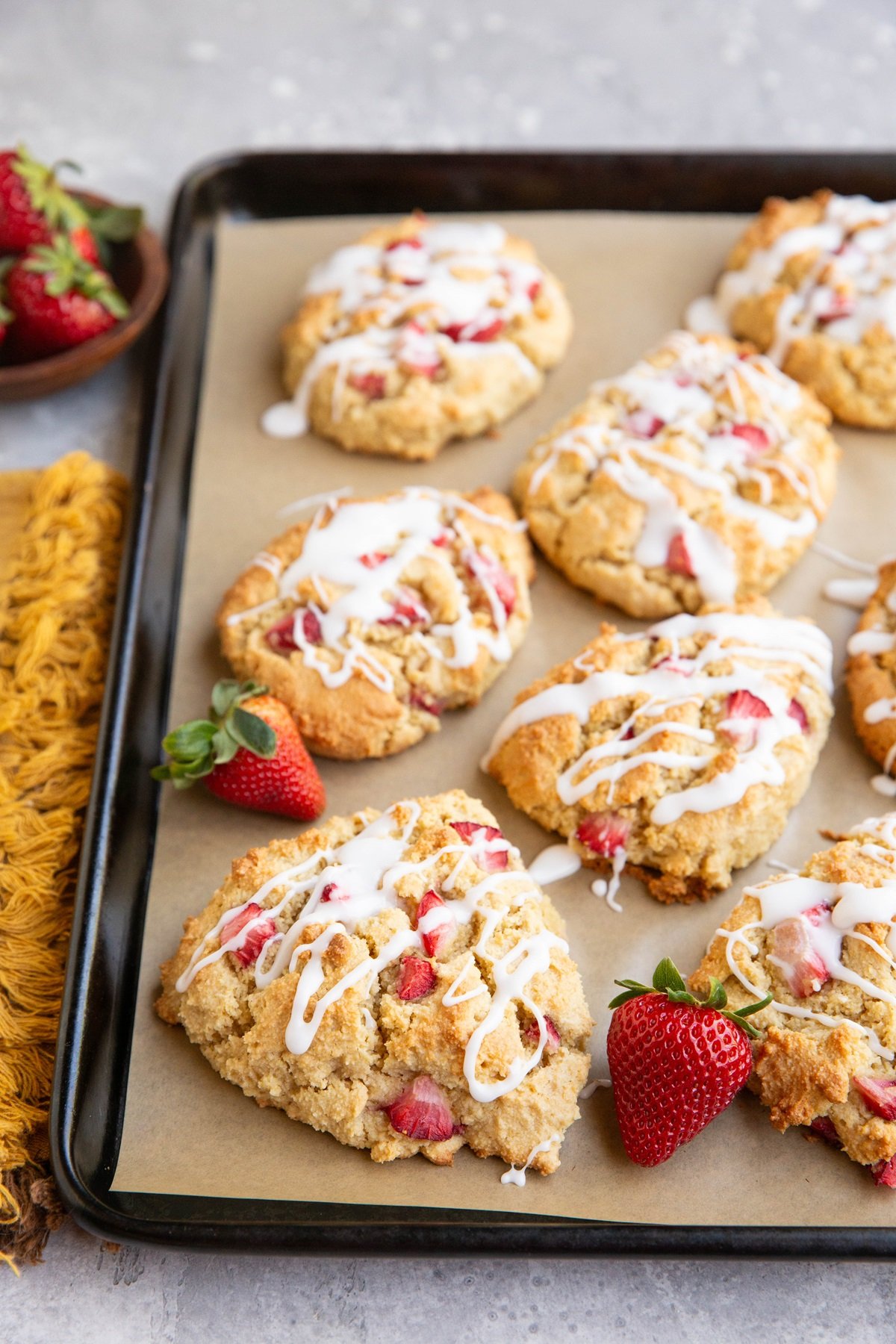 Baking sheet of almond flour strawberry scones with fresh strawberries and a napkin to the side.