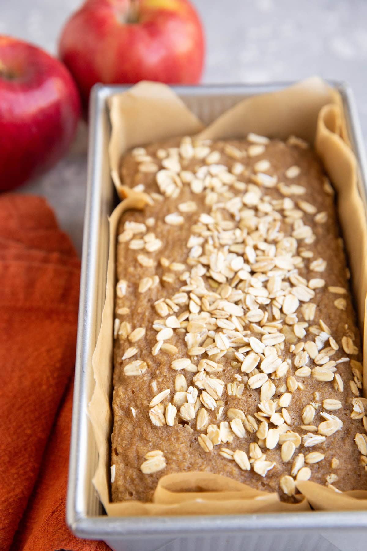 Loaf pan of applesauce bread fresh out of the oven with fresh apples in the background.