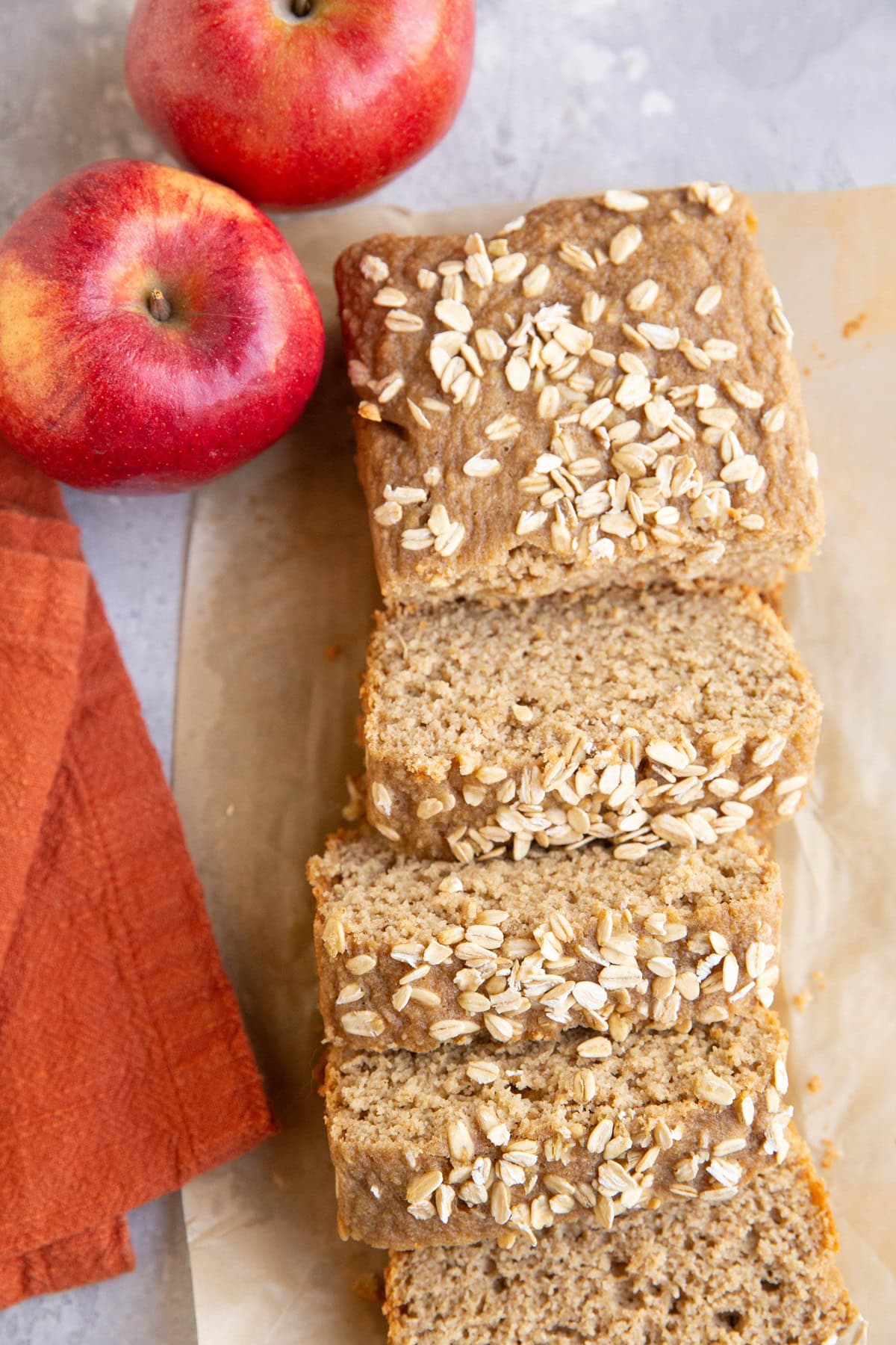 Loaf of applesauce bread on a sheet of parchment paper, cut into slices with fresh apples to the side.