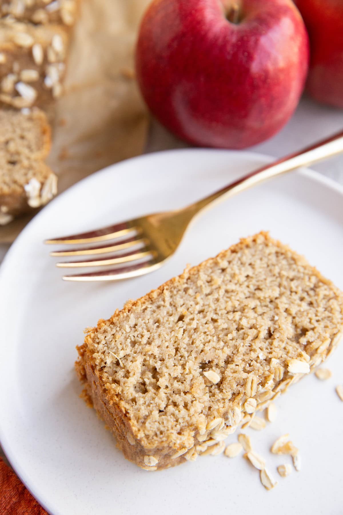 Slice of applesauce bread on a white plate with the rest of the loaf of bread in the background.