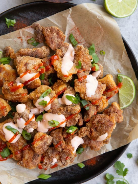 Plate of crispy bang bang chicken drizzled with sauces with fresh lime and cilantro to the side, ready to serve.