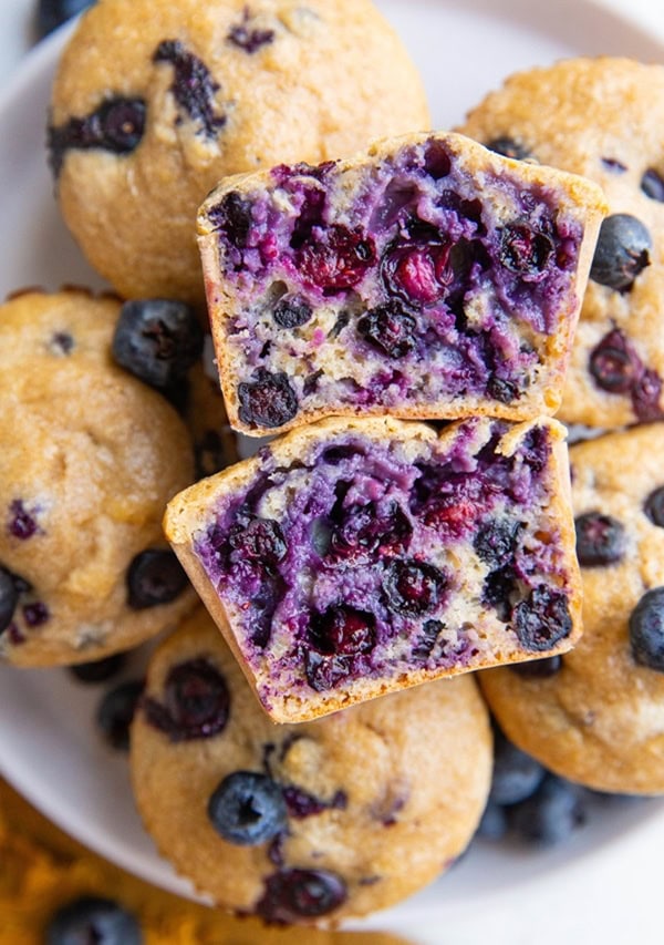 Plate of oatmeal blueberry protein muffins with one sliced in half, exposing the inside.