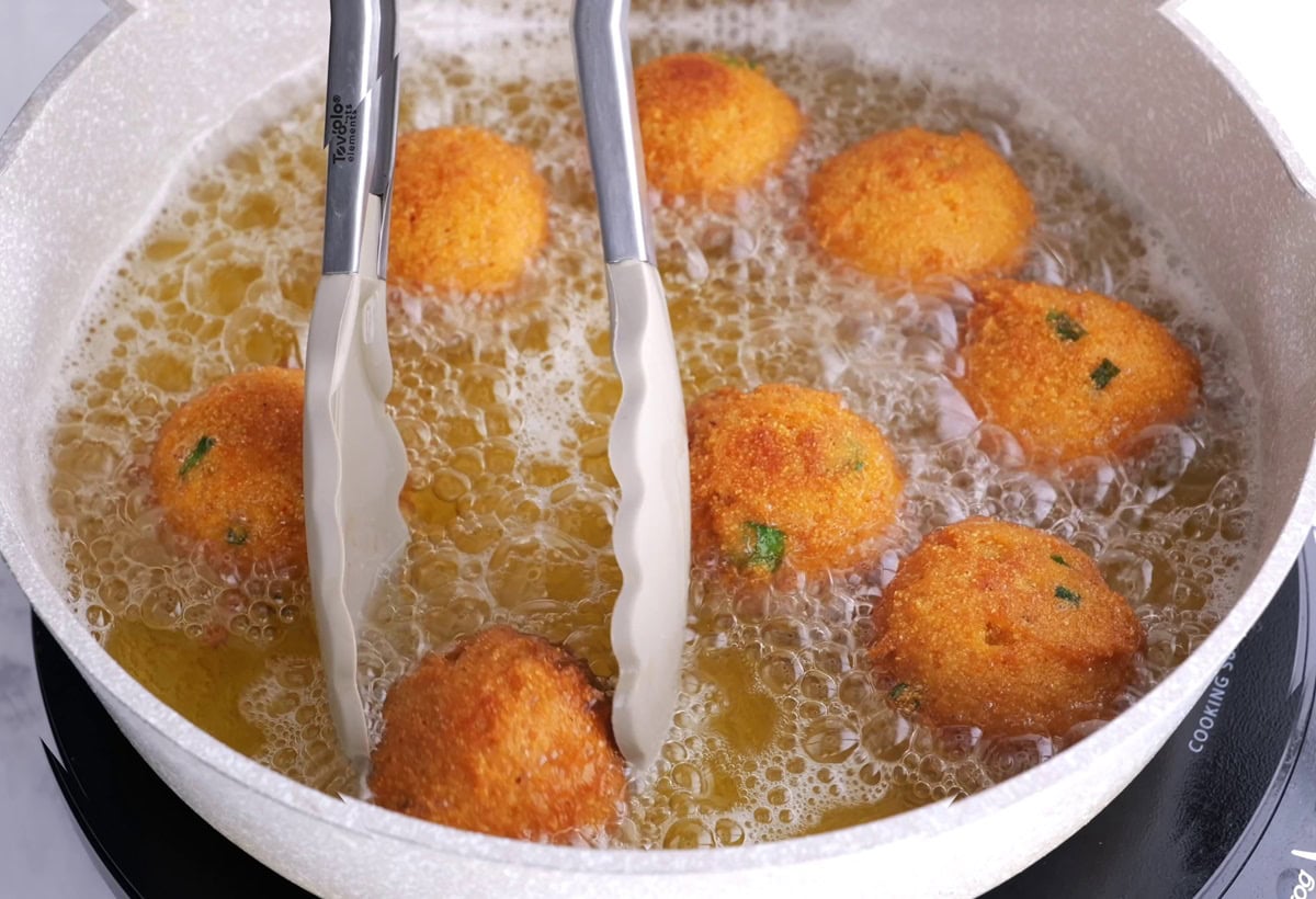 Tongs turning over hush puppies to golden brown perfection.