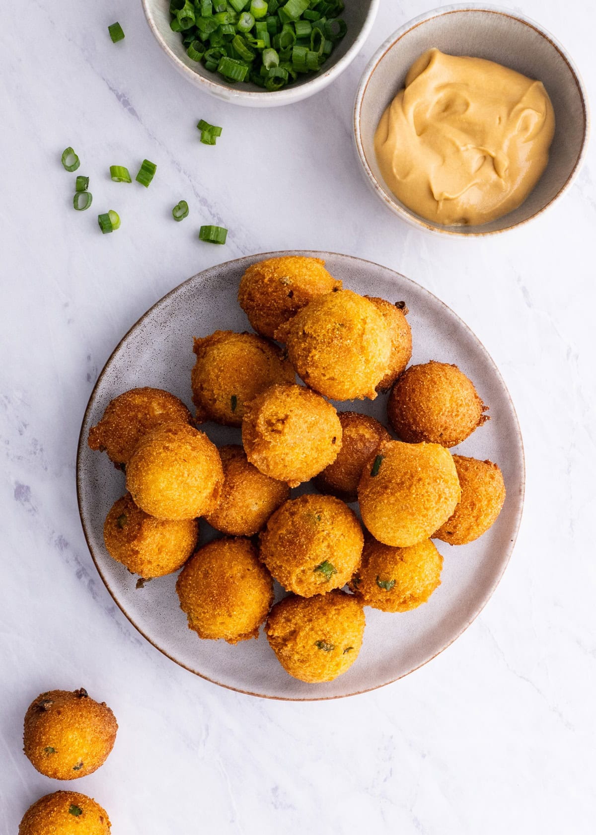 Plate of southern style hush puppies with green onions and a bowl of sauce to the side.