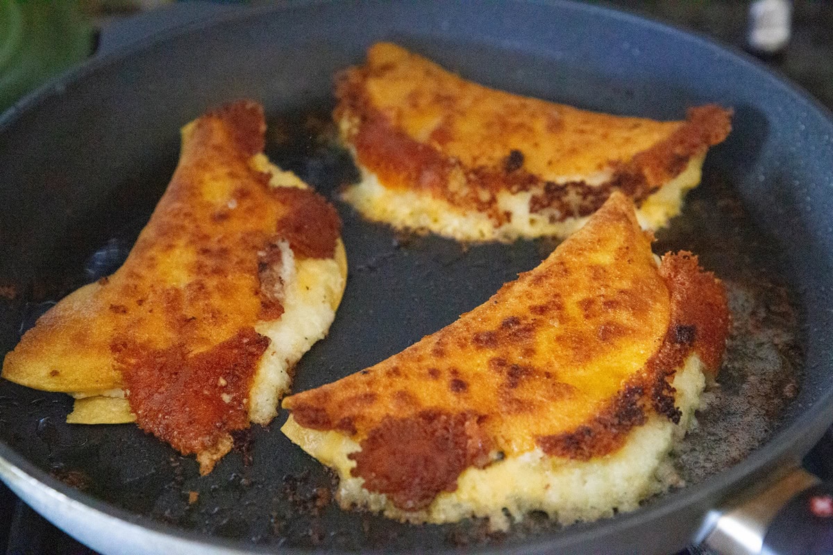 Potato tacos frying in a frying pan.