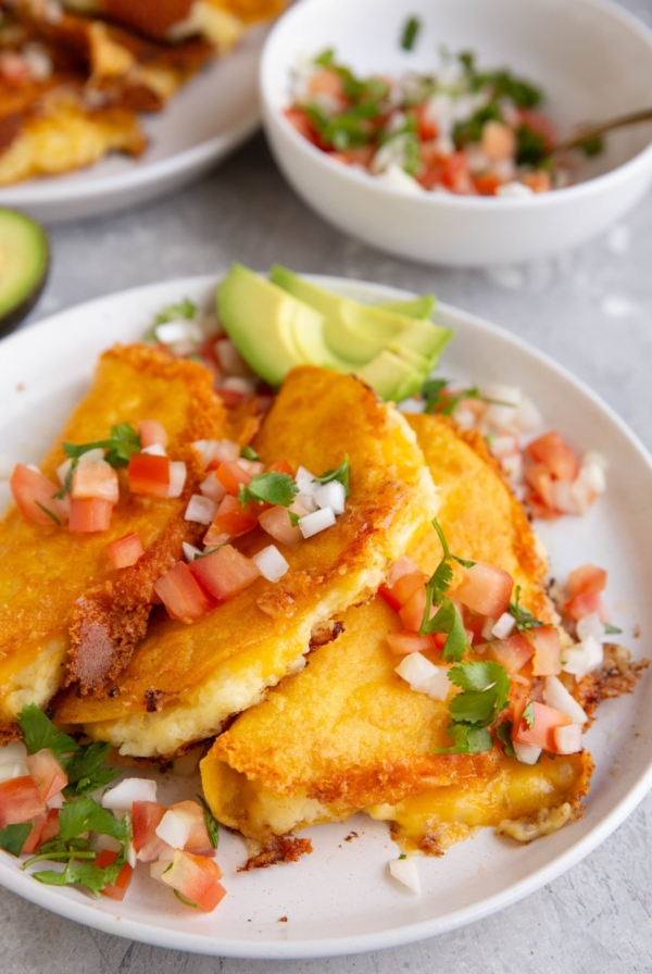 White plate of potato tacos with a bowl of pico de gallo in the background.