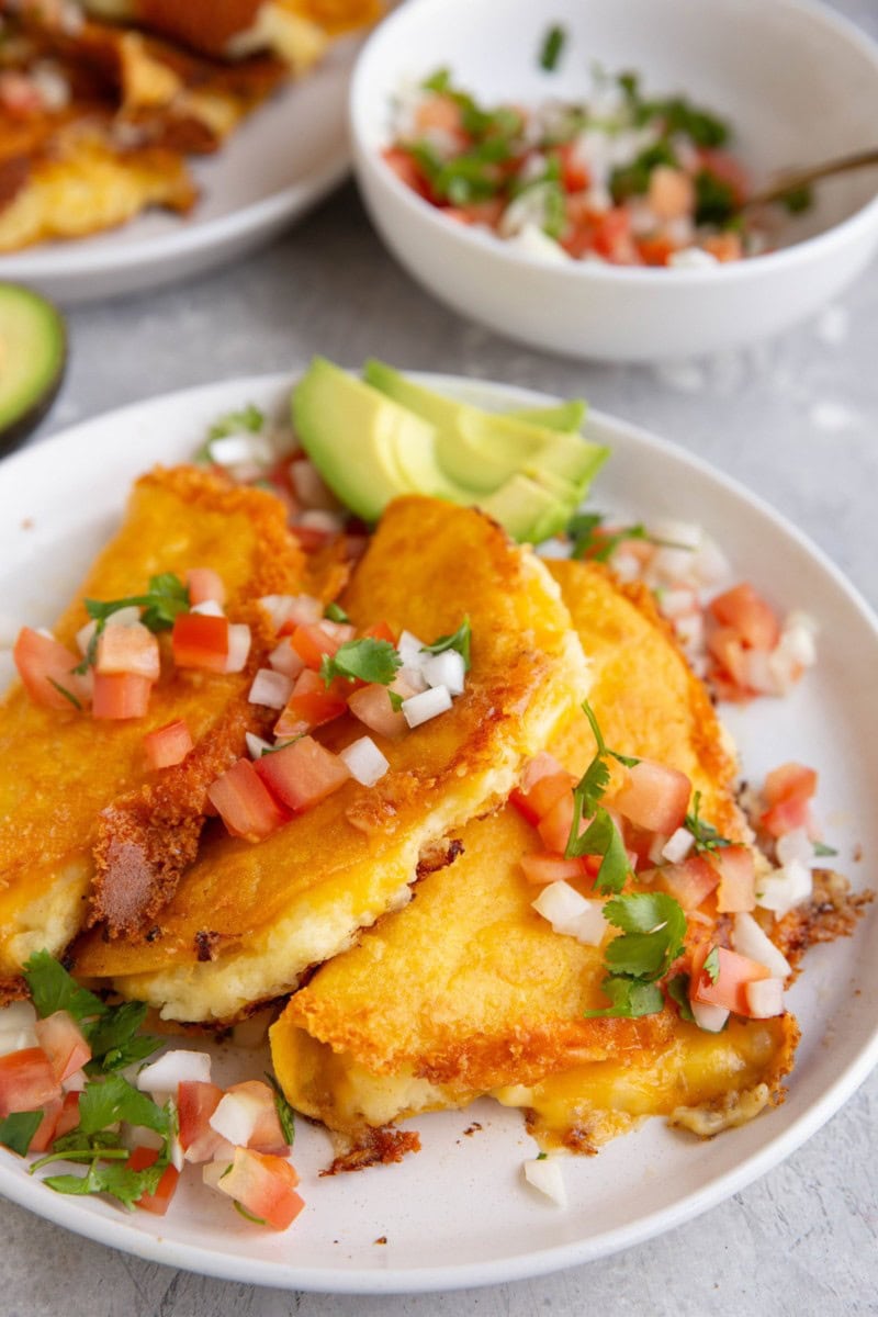White plate of potato tacos with a bowl of pico de gallo in the background.