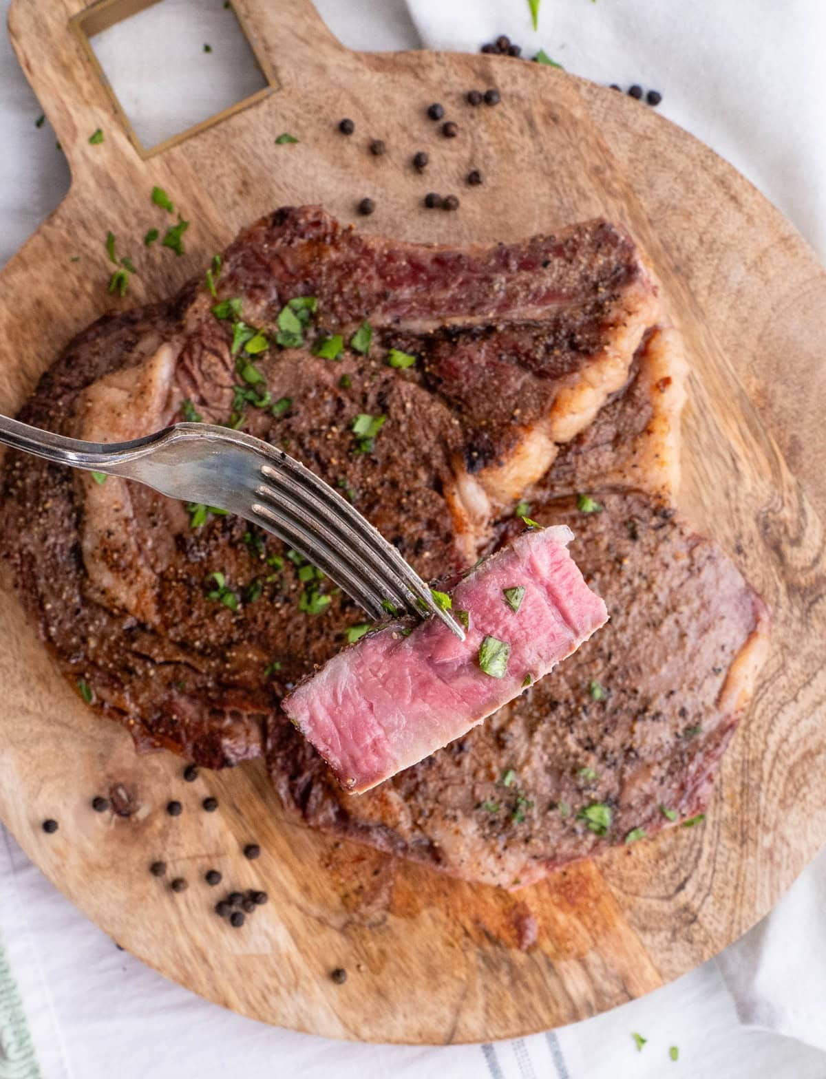Cutting board with steaks on top and a fork holding a piece of meat.