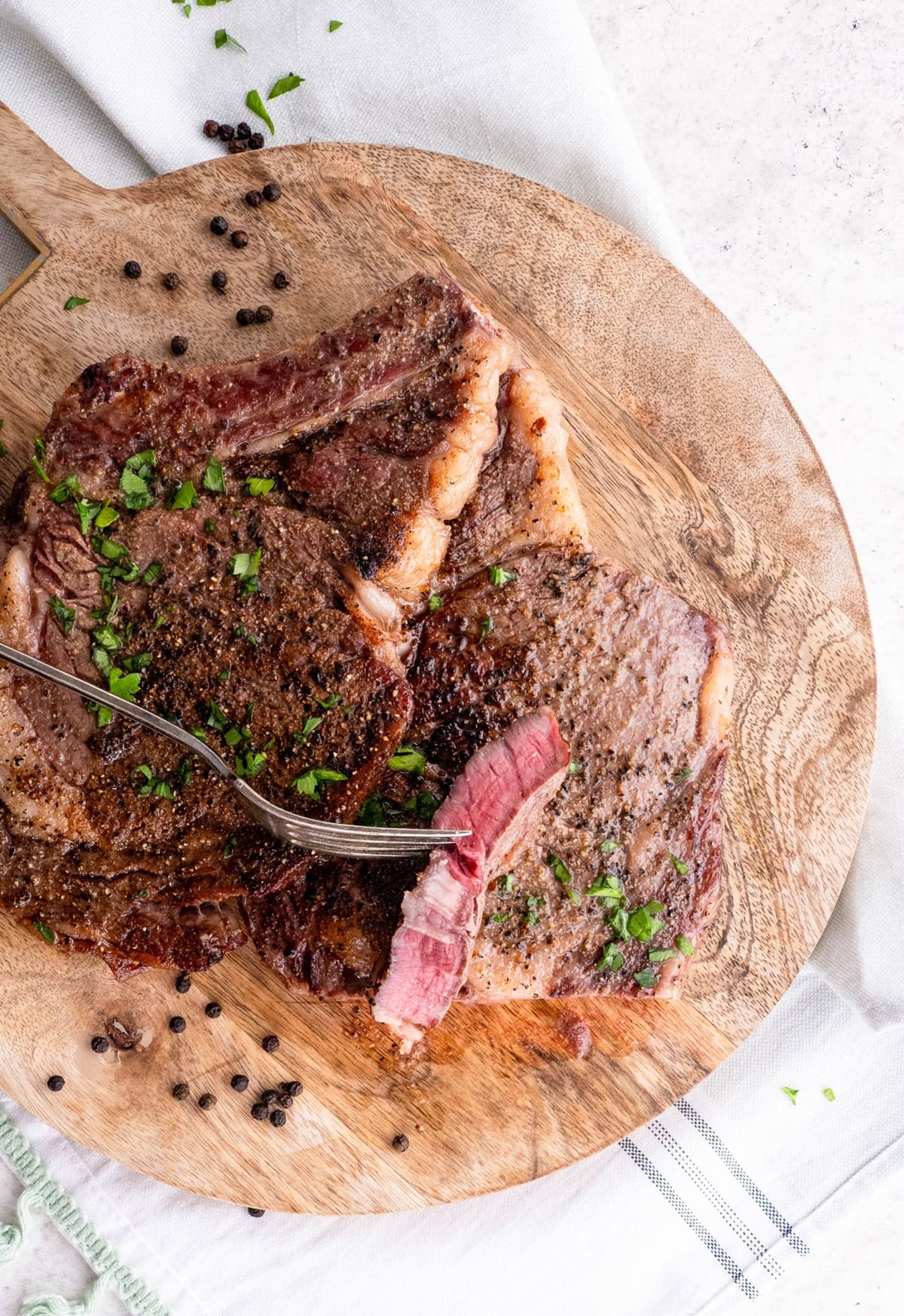 Fork holding a slice of steak with two cooked steaks underneath.