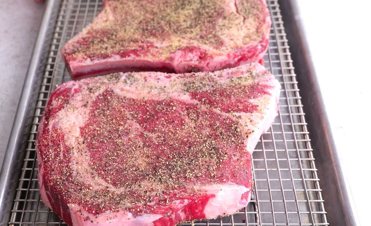 Steaks on a roasting pan with a wire rack, ready to go into the oven.