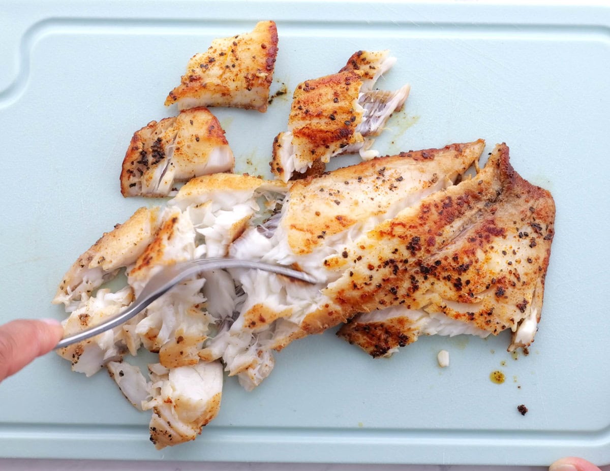 Sole filet freshly cooked on a cutting board, being shredded with a fork.