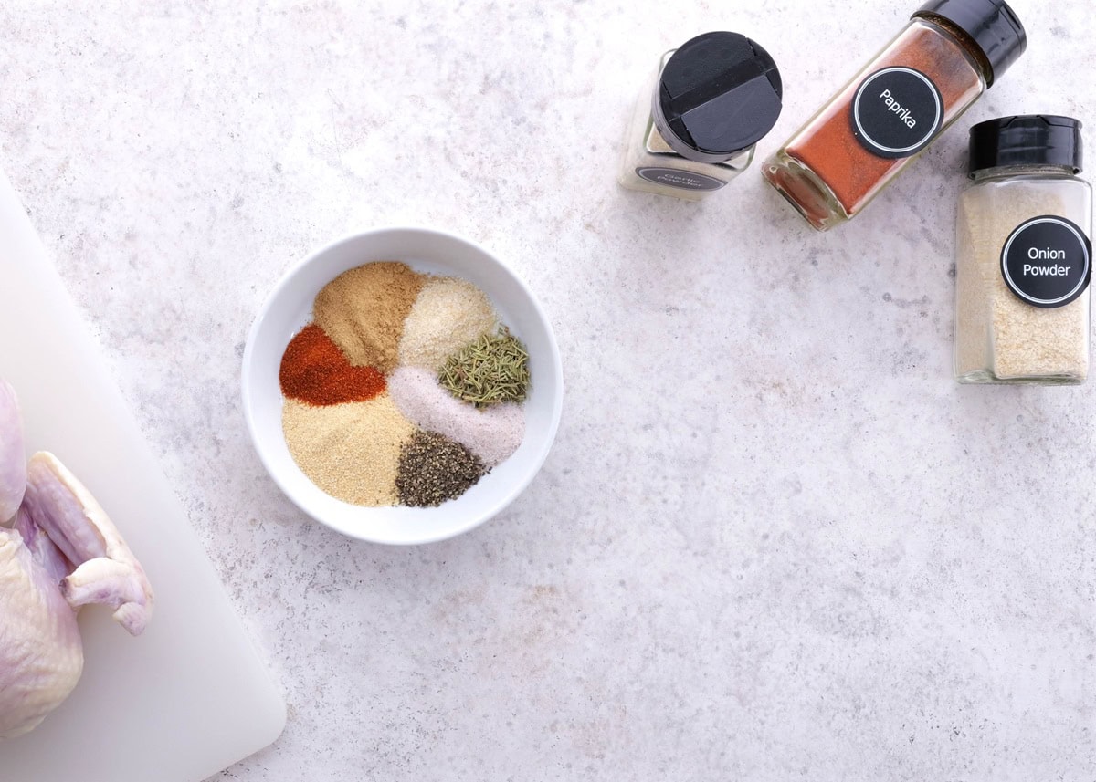 Seasonings for dry rub in a small bowl with bottles of seasonings to the side.