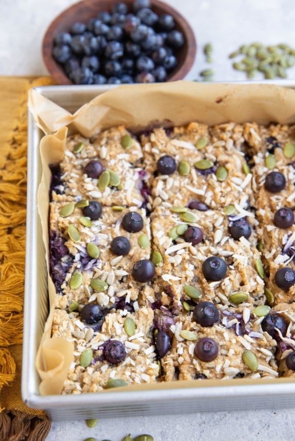 Baking dish of blueberry breakfast bars sprinkled with seeds and coconut.