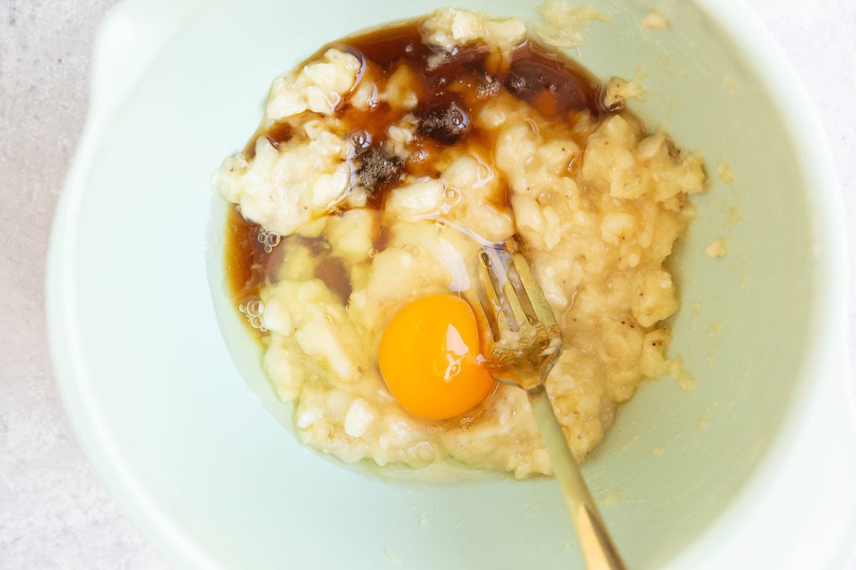 Mashed bananas, egg, and pure maple syrup in a mixing bowl to be mixed together.
