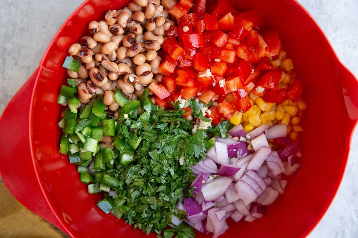 Red mixing bowl with cowboy caviar ingredients inside.